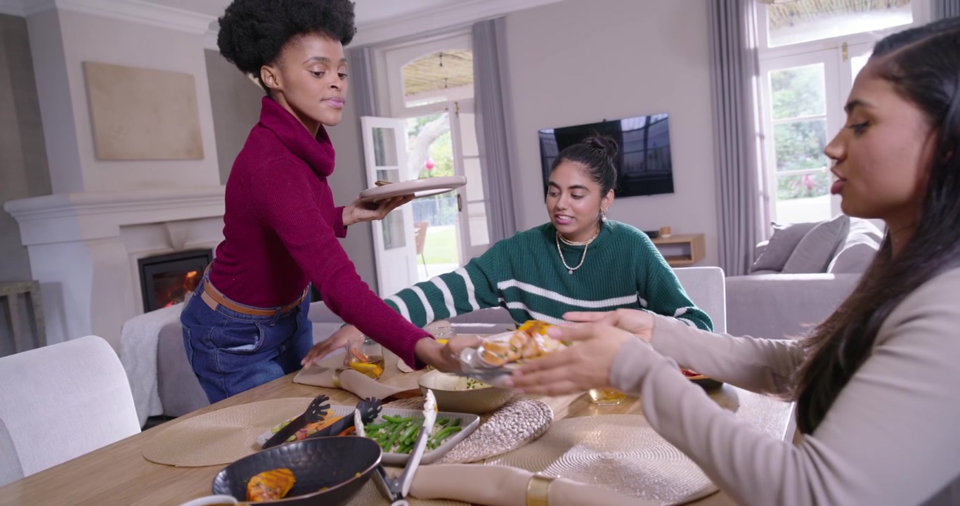 Des amies diverses terminent leur repas, se passent des assiettes, une poêle et un bol tout en débarrassant la table à manger.