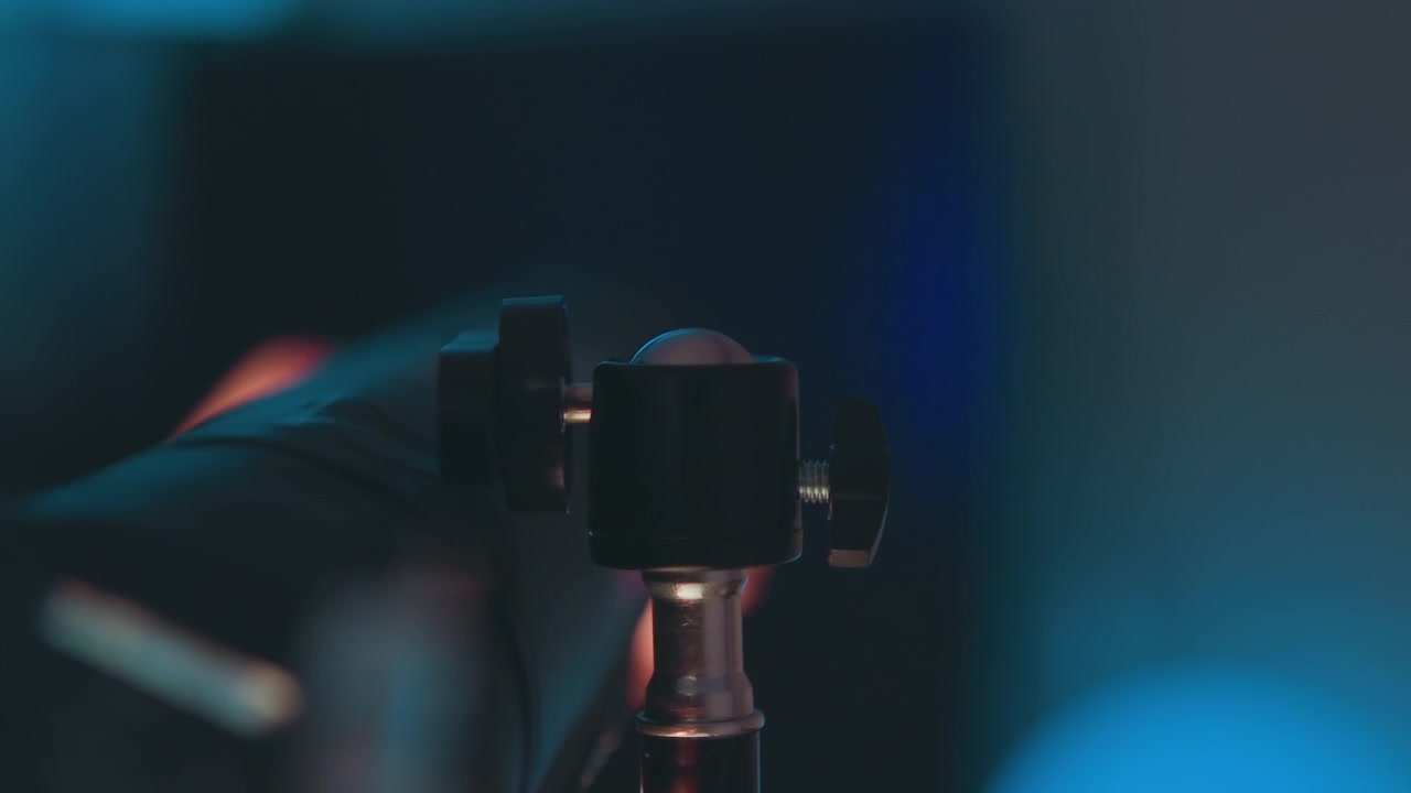 Tight view of microphone head secured to metal stand mount, showing threaded post, adjustment knob, grille, and soft studio glow with slight forward tilt suggesting adjustment and ready sound setup