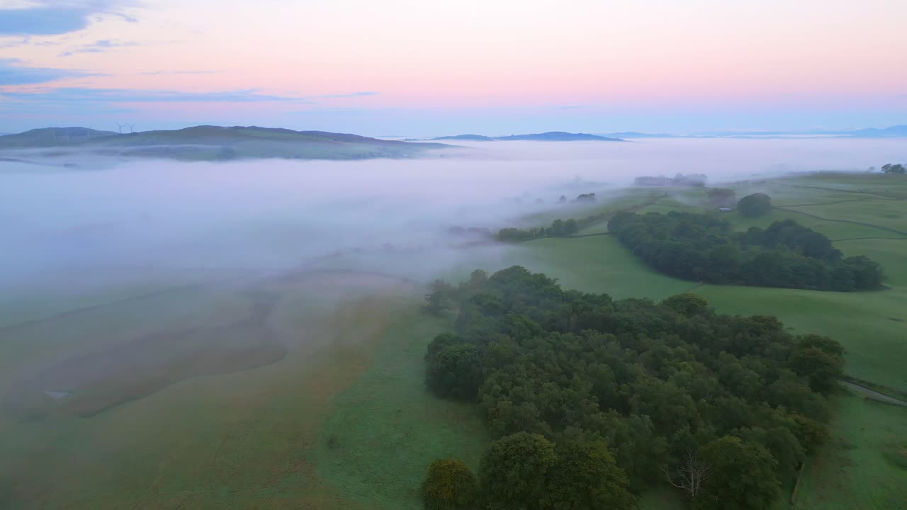 volando sobre campos verdes al amanecer hacia la niebla, el banco de niebla y las montañas lejanas con el resplandor del amanecer en el horizonte