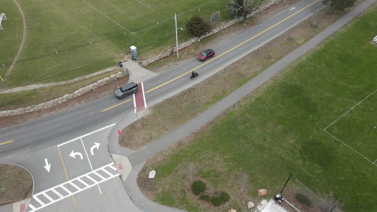 주차장을 떠나 도로를 주행하는 오토바이의 드론 추적 샷