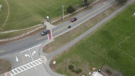 Toma-De-Seguimiento-De-Un-Dron-De-Una-Motocicleta-Que-Sale-De-Un-Estacionamiento-Y-Conduce-Por-Una-Carretera