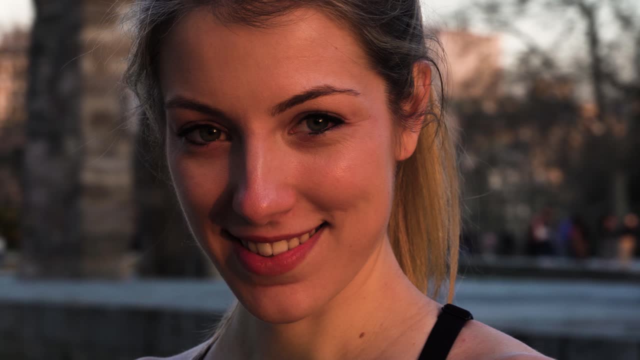 atractiva joven rubia fitness mujer sonriendo a la cámara en el parque de la ciudad