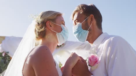 retrato de una feliz pareja de recién casados caucásicos tocando las cabezas en el altar, usando máscaras faciales