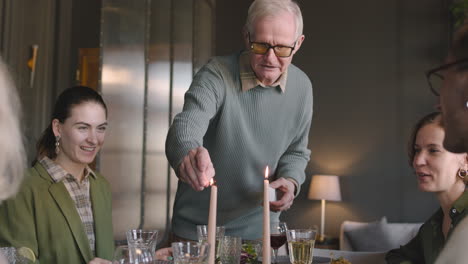 senior man lighting up candles on dining room table during family reunion at home 1