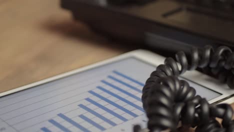 Office-phone-and-tablet-with-blue-bar-chart-displayed-on-screen-on-wooden-office-table-panning-shot