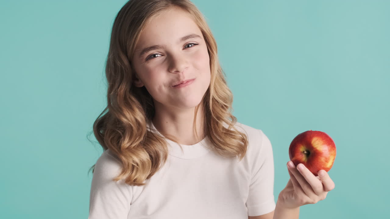 una adolescente caucásica en pijama comiendo una manzana y sonriendo.