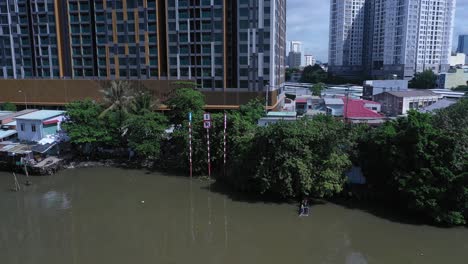 Aerial-view-on-Kenh-Te-canal-Ho-Chi-Minh-City-with-old-iron-and-wood-shacks,-traditional-river-boats-and-ultra-modern-high-rise-buildings-on-sunny-day