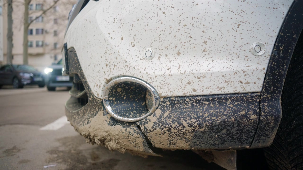 Nahaufnahme eines schmutzigen weißen Fahrzeugstoßfängers, bedeckt mit getrocknetem Schlamm, Spritzern und Straßenschmutz