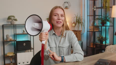 happy caucasian businesswoman talking with megaphone proclaiming news sitting at home office table