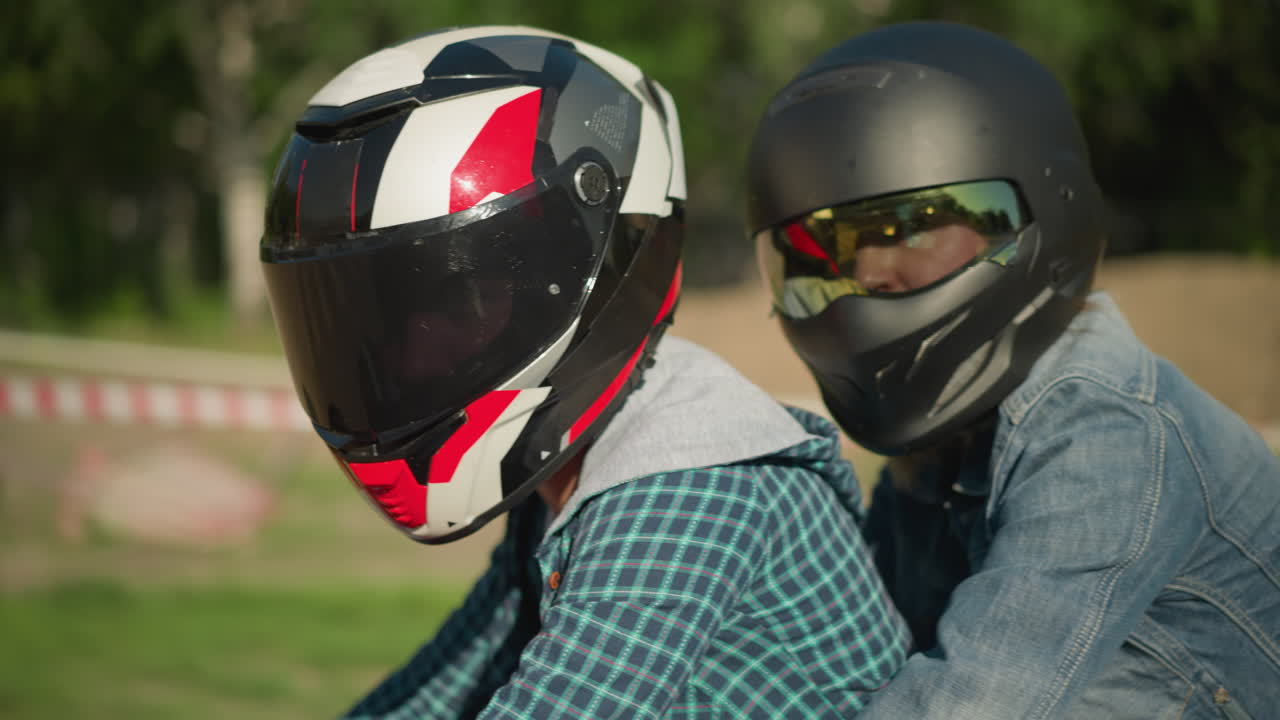dos amigos montan una bicicleta eléctrica con cascos mientras miran la cámara, el fondo está borroso, con una cinta de advertencia y coches estacionados