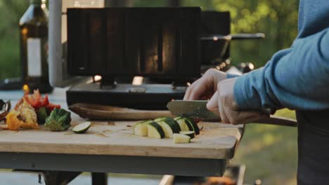 close up of man cutting vegetables on wooden board near gas stove, preparing tasty meal