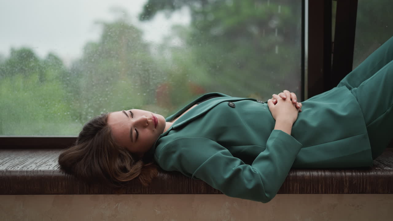 Businesswoman leans back on windowsill. Rainy weather helps to let go woman stresses plaguing mind. Finding solace in sight of world beyond office walls