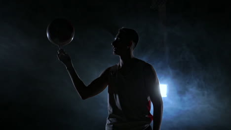 hooded basketball player spinning the ball at night in an empty car park, in slow motion