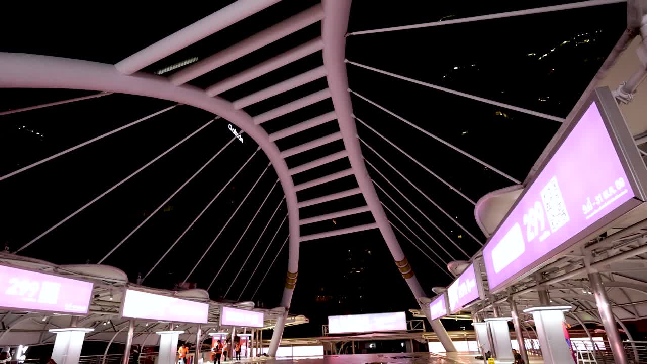 Camera tilts down revealing illuminated modern bridge structure and cityscape at night in Bangkok, Thailand
