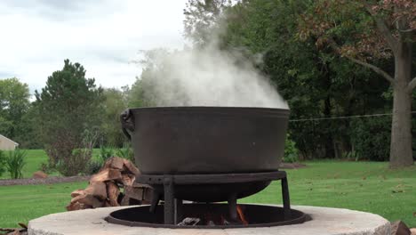 an old fashioned iron kettle over the fire of an outdoor campfire