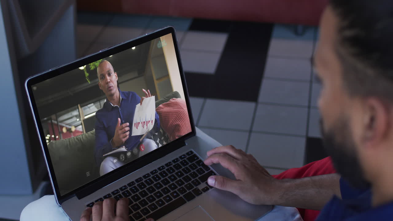 African american man having a video call with male office colleague on laptop at home