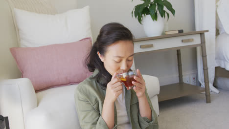 happy asian woman drinking tea in bedroom, in slow motion