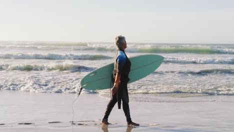 senior african american woman walking with a surfboard at the beach