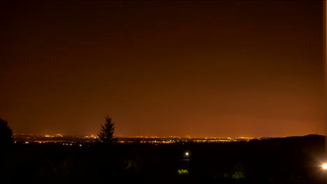 Cielo-Nocturno-Estrellado-De-Lapso-De-Tiempo-Y-Ciudad-Distante-Naranja-Brillante