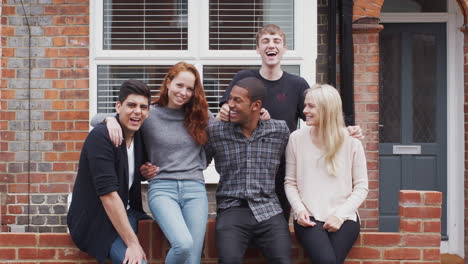 outdoor portrait of student friends sitting on wall outside shared house together