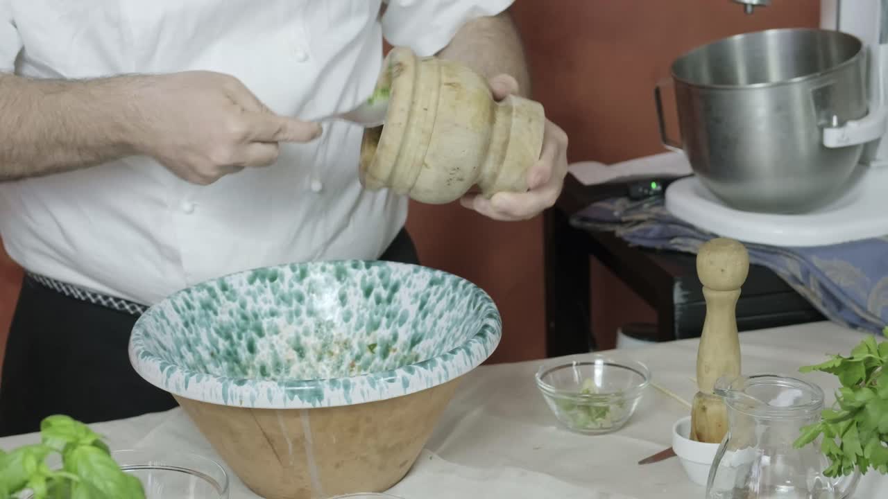 Chef scrapes side of wooden mortar with metal spoon to remove freshly crushed nuts