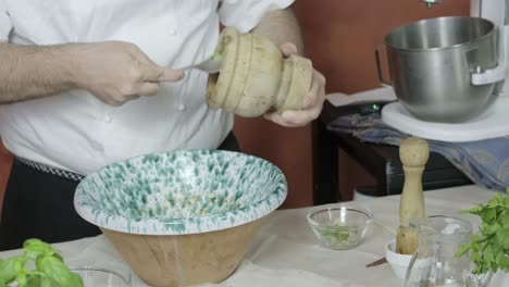 el chef raspa el lado del mortero de madera con una cuchara de metal para eliminar las nueces recién trituradas