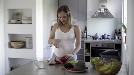 mujer embarazada joven alegre cocinando en la cocina