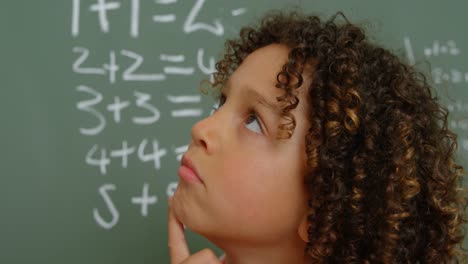 Close-up-of-thoughtful-mixed-race-schoolgirl-with-hand-on-chin-standing-in-classroom-at-school-4k