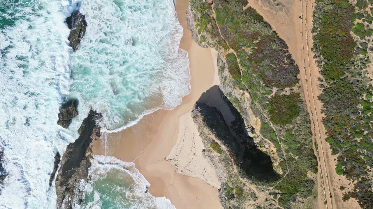 Waves crash on golden sand by cliffs, Praia de Samoqueira, Alentejo, Portugal