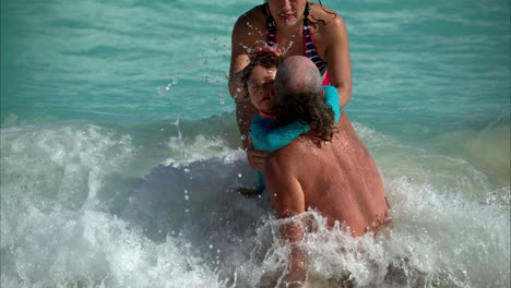 Eine-Dreiköpfige-Mexikanische-Lateinamerikanische-Hipster-Alternative-Familie-Sitzt-Auf-Dem-Sand-Und-Wird-Von-Einer-Welle-Zerschmettert,-Die-Spaß-An-Einem-Strand-In-Cancun,-Mexiko-Hat