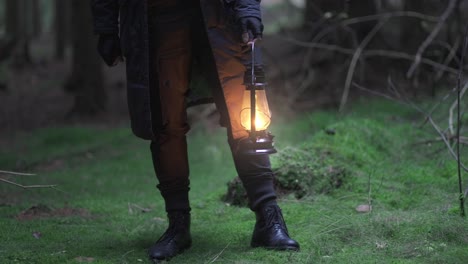 Close-up-shot-of-male-hands-carrying-a-lit-up-lantern-in-the-middle-of-a-forest-during-evening-time