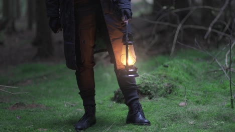 close up shot of male hands carrying a lit up lantern in the middle of a forest during evening time