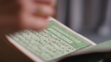 close up of person turning pages of the quran on stand at home