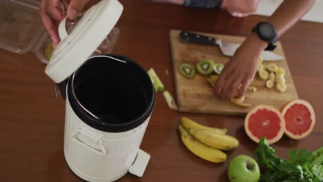 Hands-of-biracial-man-composting-vegetable-waste-in-kitchen