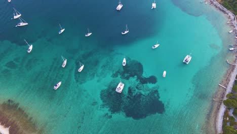 Boats-in-a-bay-near-the-coastal-city-of-Croatia-against-a-background-of-blue-sky-and-blue-transparent-water-and-houses-with-red-roofs