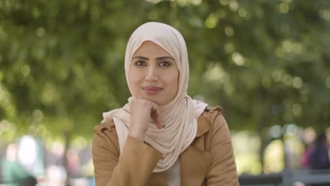 Portrait-Of-Smiling-Muslin-Woman-Wearing-Hijab-Sitting-At-Outdoor-Table-On-City-Street