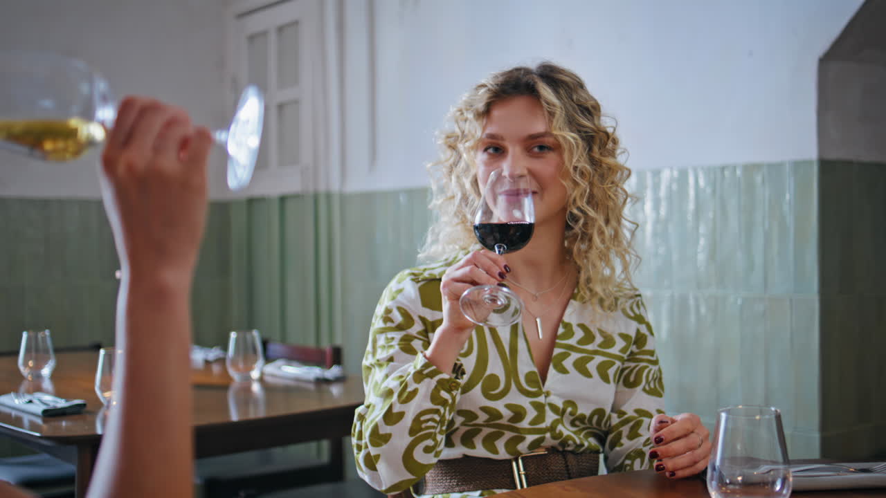 To kvinner som drikker vin og ler mens de ser på en mobiltelefon på nært hold i en koselig restaurant
