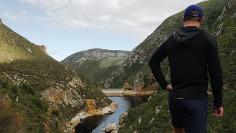 Junges-Männchen-Steht-An-Einem-Aussichtspunkt-In-Den-Bergen-Mit-Blick-Auf-Ein-Wasserreservoir-Mit-Dunklem,-Nährstoffreichem-Wasser,-Naturschutzgebiet-Fernkloof,-Hermanus,-Südafrika