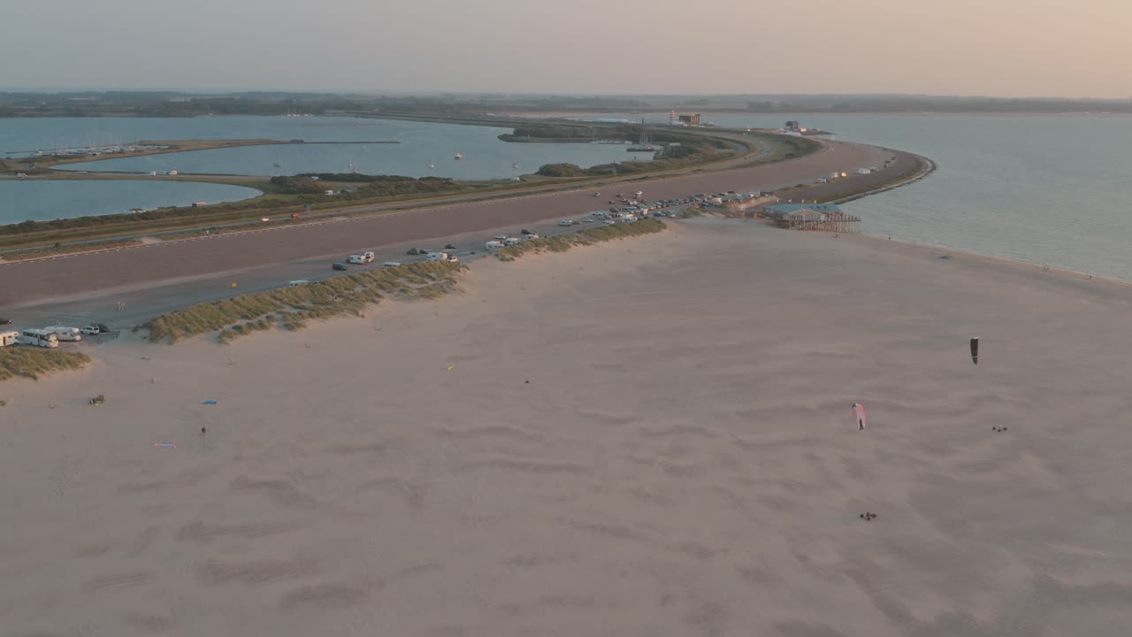 drone cinemático - toma aérea de la playa natural verde y arenosa al atardecer con turistas y personas con buggykiting en zelanda en el mar del norte, países bajos, 30p