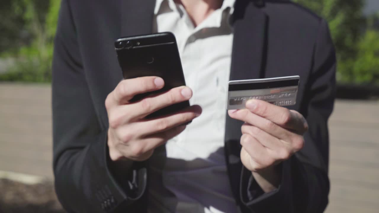 manos masculinas jóvenes poniendo datos de tarjetas bancarias en el teléfono, pagando en línea