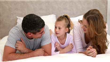 padres y hija acostados en la cama charlando