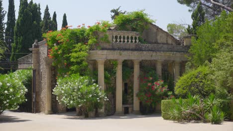 amidst the garden, an old stone structure with columns is depicted