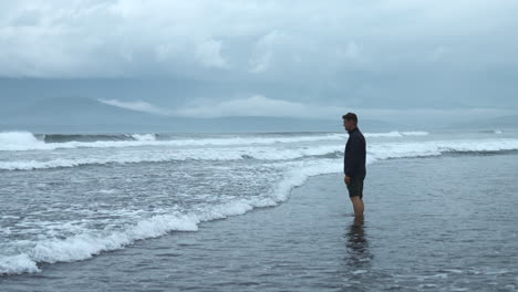 man standing in the surf on a cloudy day