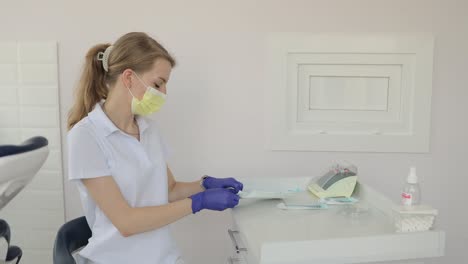 a woman, with her gloves and mask, sits at a dental office table, ready for service, showcasing a cautious gesture.