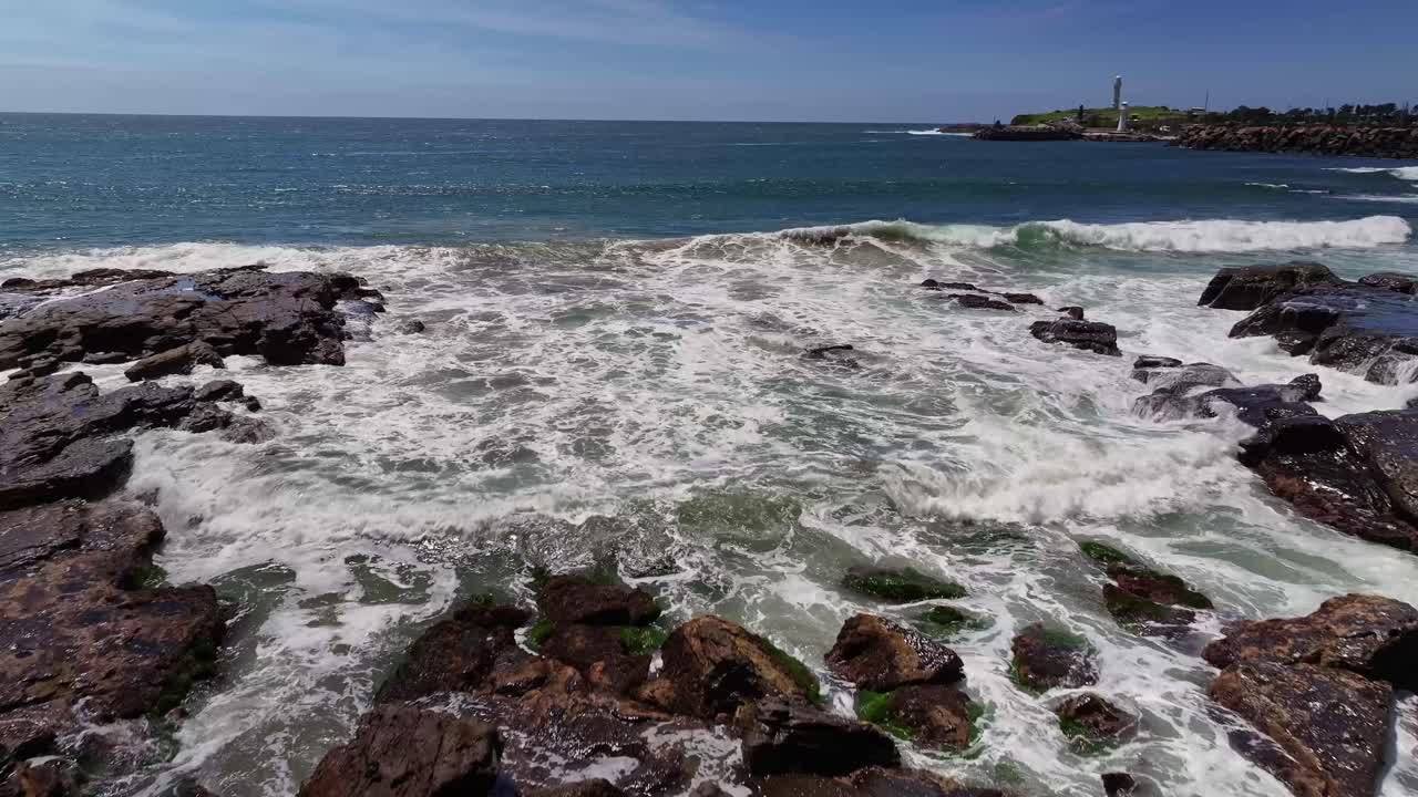 aérea sobre rocas dentadas y el surf hacia los faros en el puerto de wollongong más allá