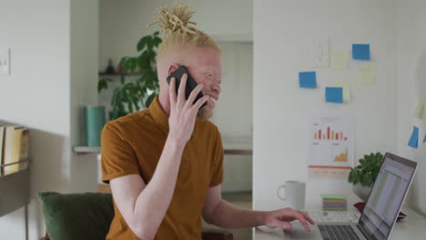 Albino-african-american-man-with-dreadlocks-working,-using-laptop-and-smartphone