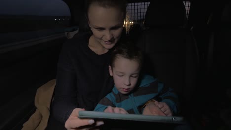 Madre-E-Hijo-Jugando-Con-El-Panel-Táctil-Durante-El-Viaje-Nocturno-En-Auto