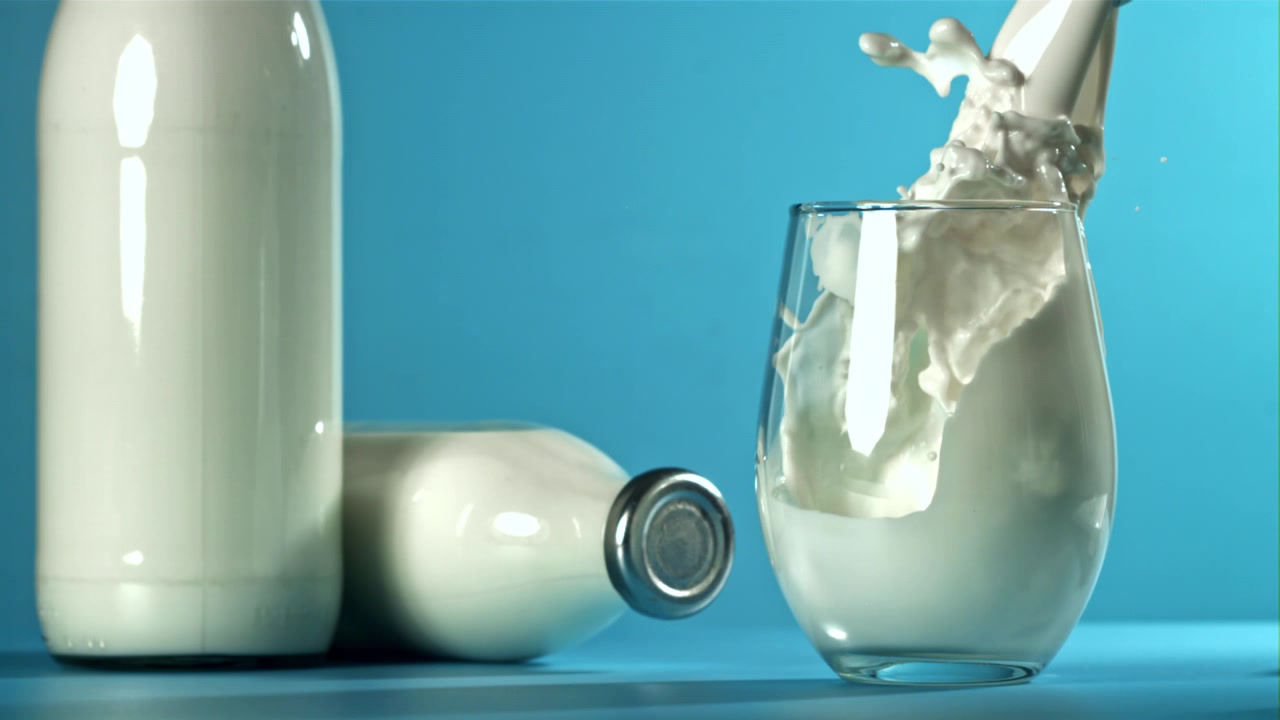 Vertiendo leche en un vaso en cámara lenta con fondo azul