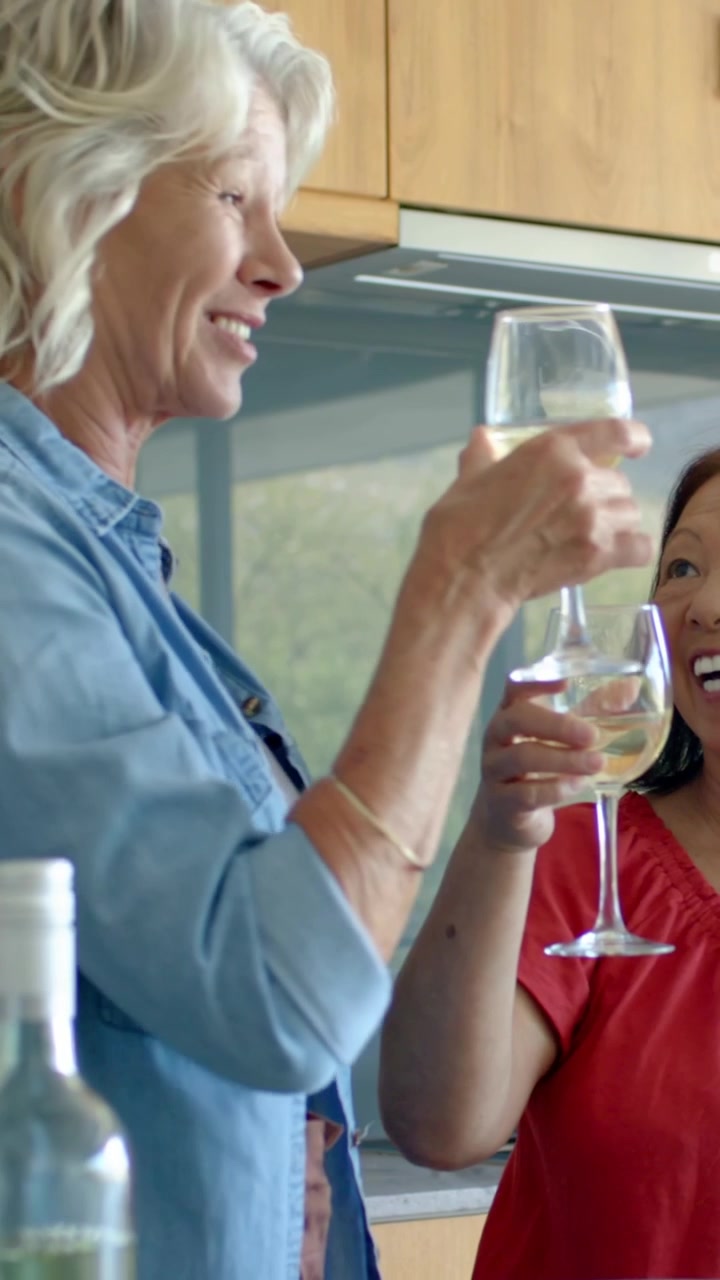 Vertical video: Cueing centered woman in red top and friends toasting in kitchen, bottle visible