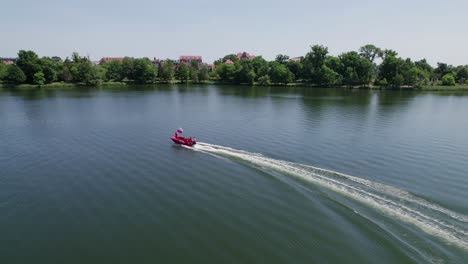 Boy-holds-polish-national-flag-on-front-of-the-red-motorboat,-epic-following-drone-shot